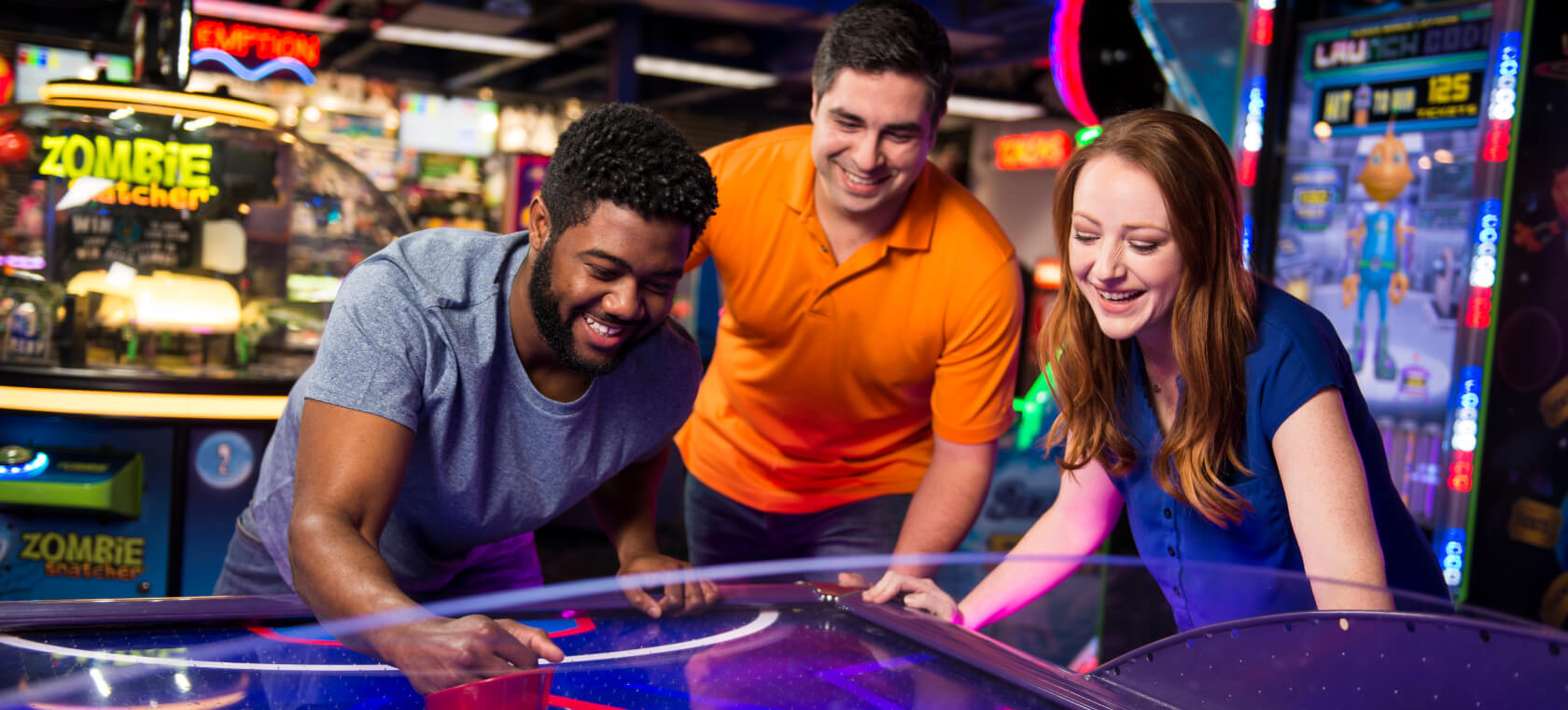 Three adults playing air hockey