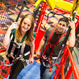 Two adults climbing up to the ropes course
