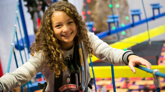 Girl smiling as she climbs the ropes course