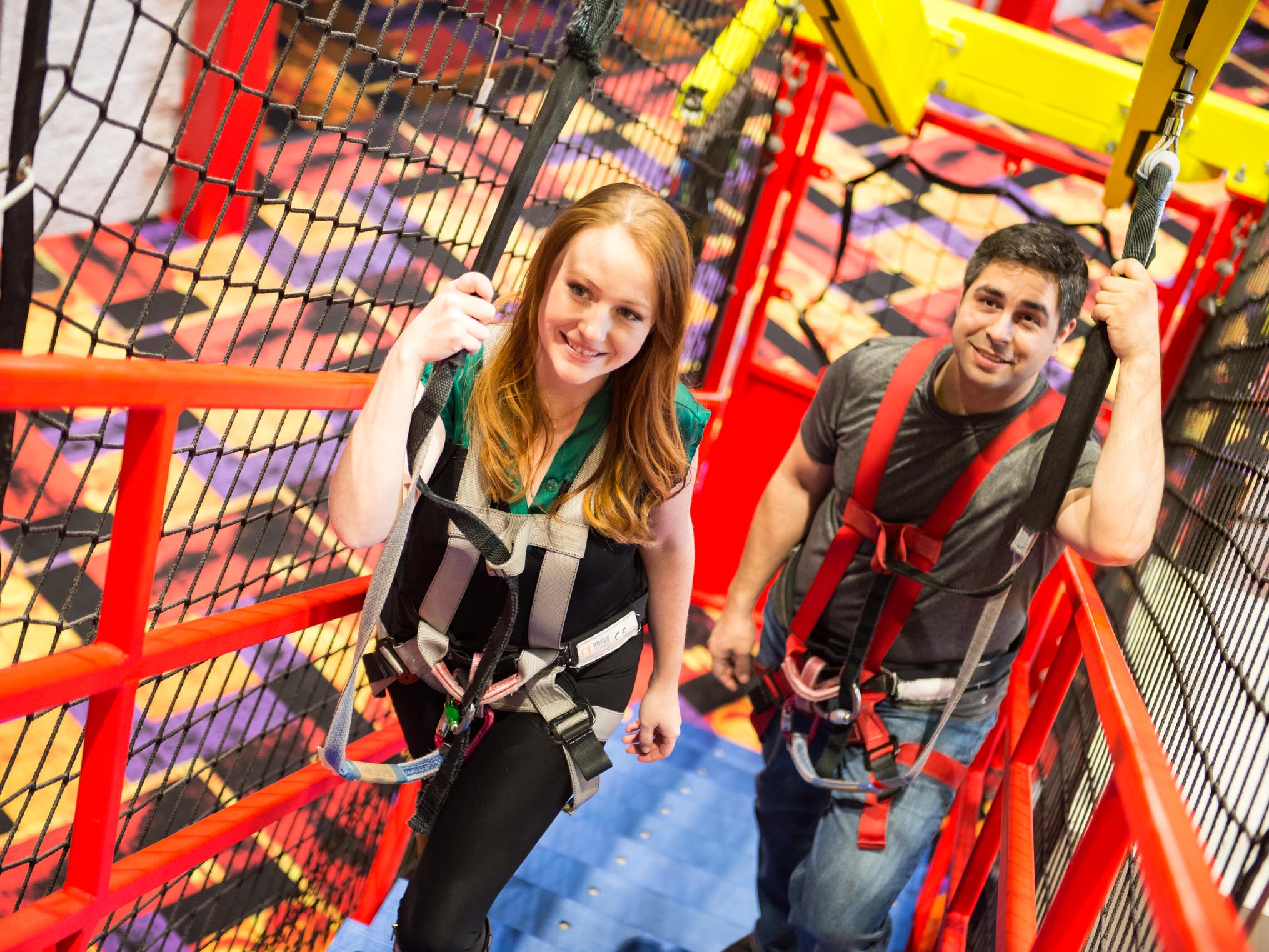 Two adults in harnesses walking up the stairs to the ropes course