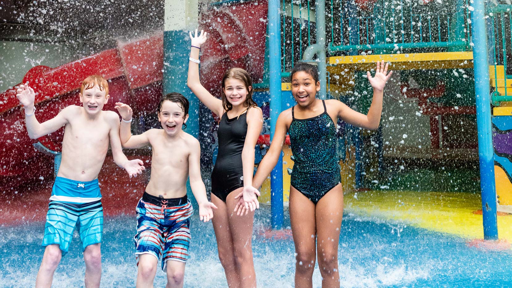 Four young kids getting water dumped on them in aquaplay