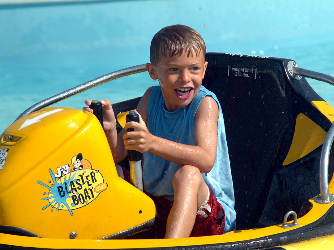 Young boy soaking wet in a bumper boat smiling