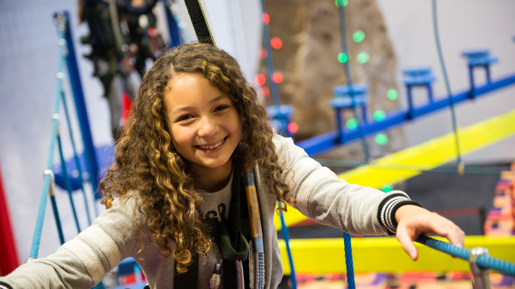 Young girl climbing through the ropes course smiling