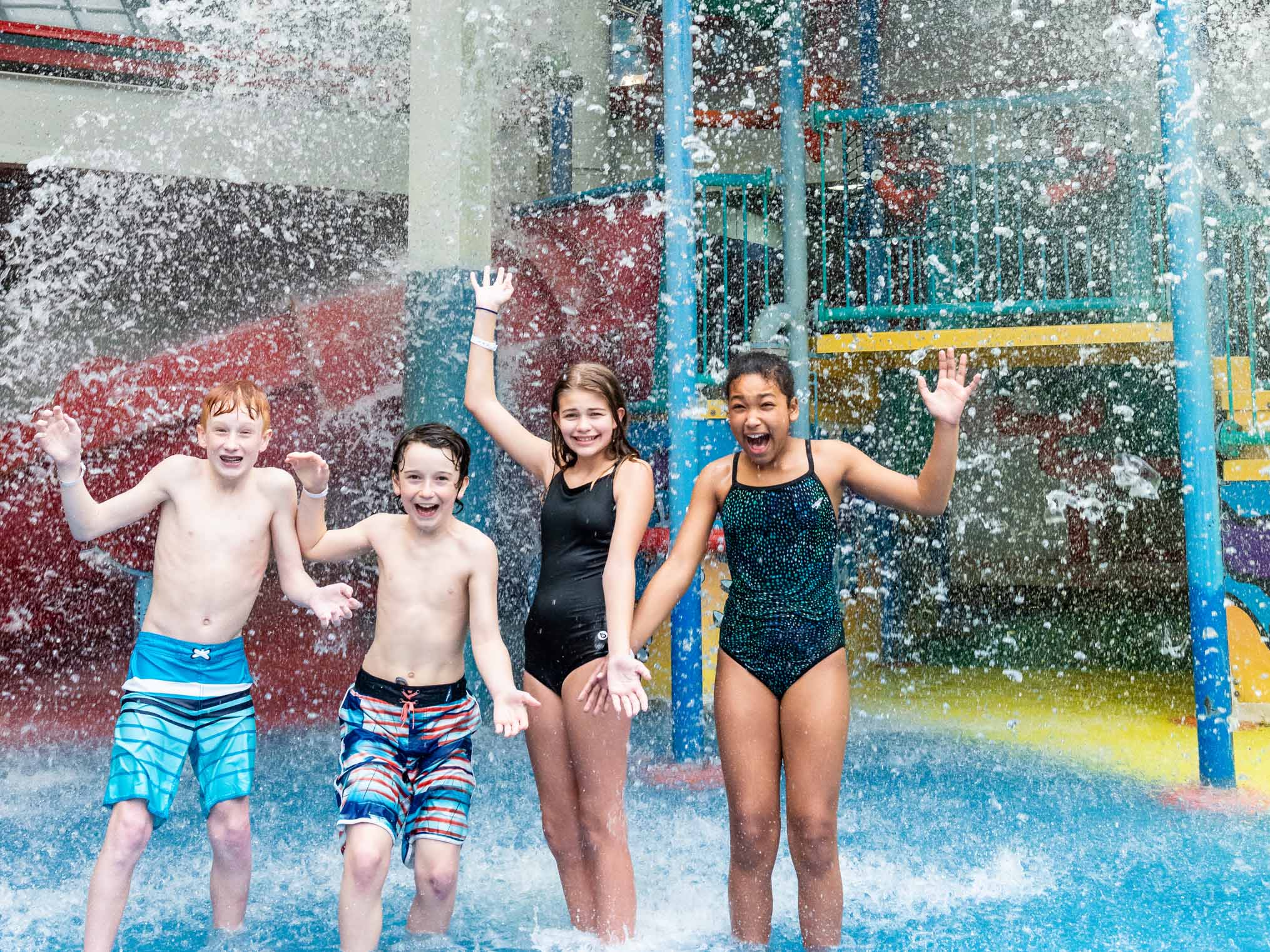 Four young friends in the aquaplay area getting splashed by water