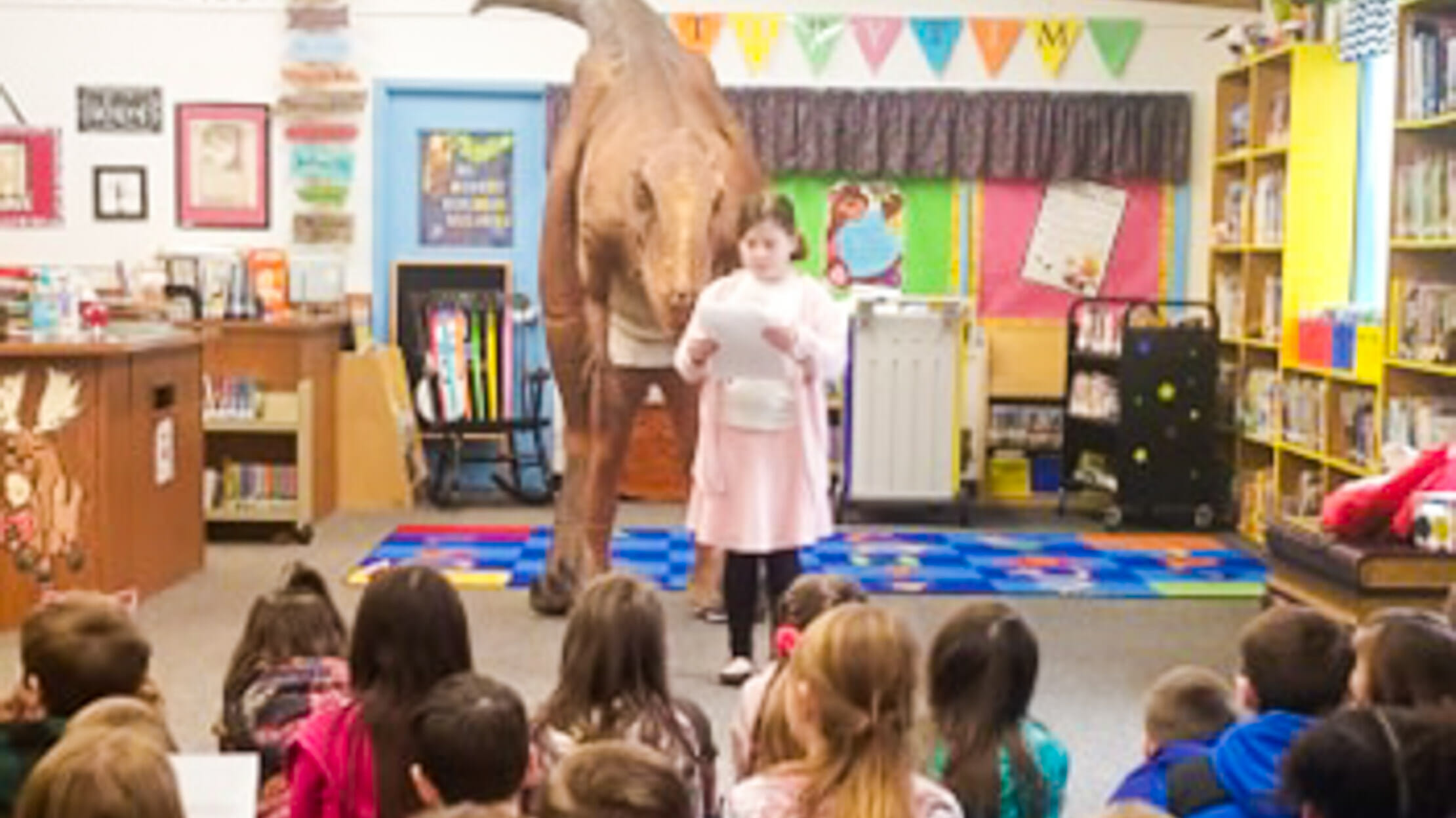 Stanley in a classroom with a young girl reading a paper in front of him to her class